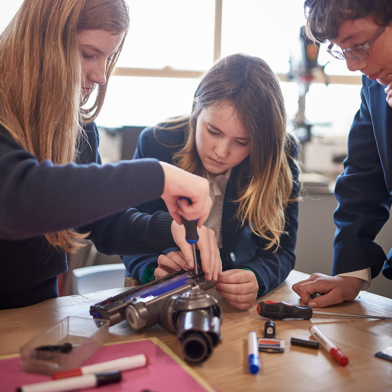 Three students using a screwdriver to take apart a Dyson vacuum cleaner machine head - an activity from the James Dyson Foundation Engineering Box.