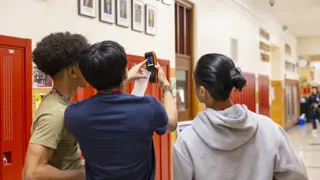 Three students using the air quality monitoring device in the hallway of their school.